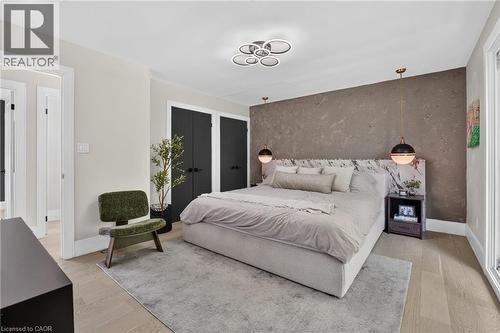 Bedroom featuring light wood-finish flooring, a textured accent wall, dual black wardrobe doors, and a modern ceiling fixture - 9 Leslie Drive, Hamilton, ON - Indoor Photo Showing Bedroom