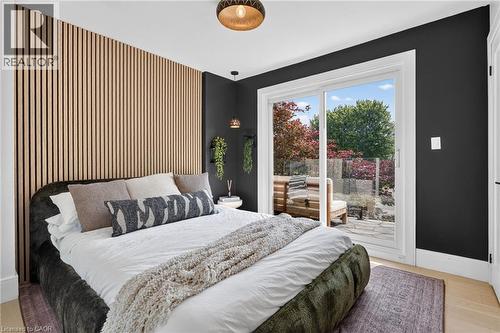 Bedroom with a slatted wood accent wall, light wood-finish flooring, and a sliding glass door leading to a stone patio - 9 Leslie Drive, Hamilton, ON - Indoor Photo Showing Bedroom
