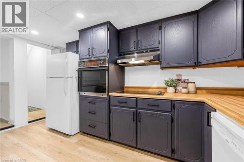 Kitchen featuring dark-toned cabinetry with decorative trim, wood-finish countertops, built-in wall oven, stainless steel range hood, and light wood-finish flooring - 11 Ford Street, Hamilton, ON 