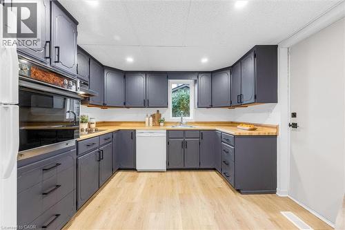 Kitchen featuring dark gray cabinetry, natural wood-finish countertops, and light wood-finish flooring - 11 Ford Street, Hamilton, ON 