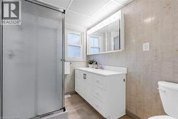 Bathroom featuring a textured glass shower enclosure with chrome framing, a white vanity with integrated sink, a mirrored medicine cabinet with integrated lighting, a window with frosted glass, and ne - 