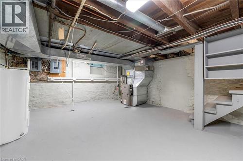 Basement area featuring a light gray floor, white painted stone foundation walls, exposed ceiling joists, and a built-in staircase with shelving - 11 Ford Street, Hamilton, ON 