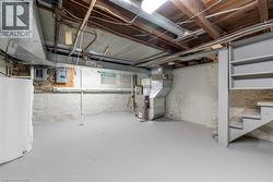 Basement area featuring a light gray floor, white painted stone foundation walls, exposed ceiling joists, and a built-in staircase with shelving - 
