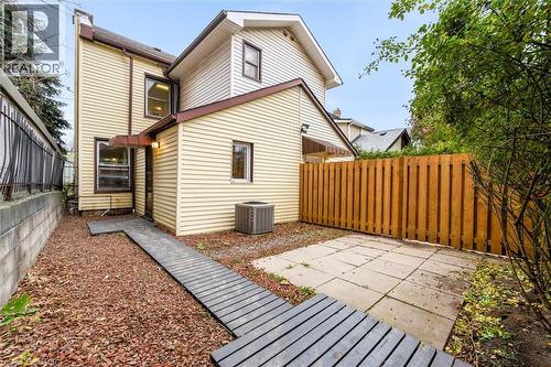 Rear exterior featuring horizontal siding, a wooden privacy fence, a concrete block retaining wall, a paved patio area, and a wood-finish pathway - 11 Ford Street, Hamilton, ON 