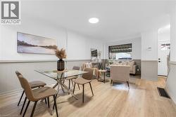 Open-concept living area featuring light wood-finish flooring, white and light grey wainscoting, a large front window, recessed lighting, and a white entry door with a frosted glass pane - 