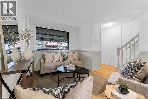 Living area featuring wood-finish flooring, a large window, a chair rail, and a visible staircase with painted handrail and balusters - 11 Ford Street, Hamilton, ON 