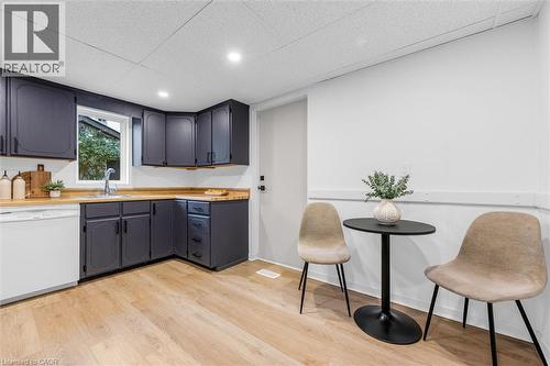 Kitchen space featuring dark cabinetry with black hardware, light wood-finish countertops, stainless steel sink with a gooseneck faucet, white dishwasher, and wood-finish flooring - 11 Ford Street, Hamilton, ON 