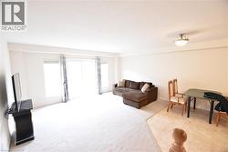 Spacious room featuring light-colored carpeting, white walls, and a large sliding glass door opening to the exterior - 
