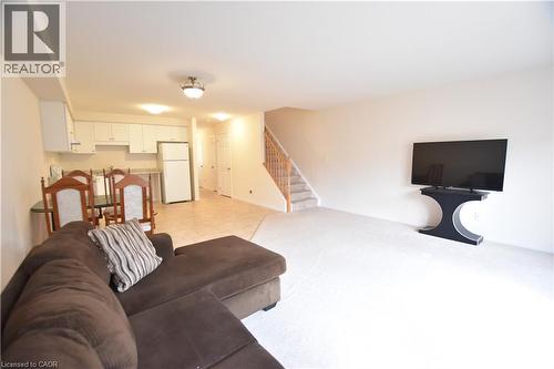 Open-concept living space featuring light-toned carpeting, a kitchen area with white cabinetry and a full-size refrigerator, and stairs with a wooden handrail - 52 Meadowridge Street, Kitchener, ON 