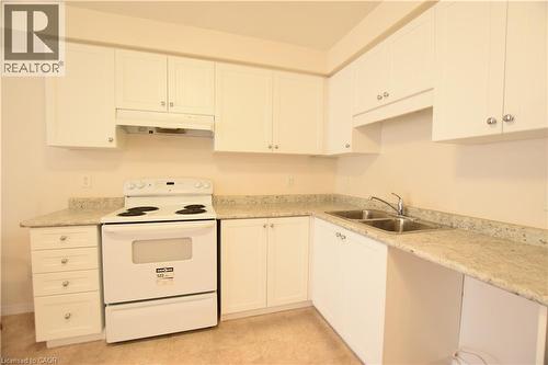 Kitchen featuring white cabinetry, light-toned countertops, a built-in range, and a double-basin stainless steel sink - 52 Meadowridge Street, Kitchener, ON 