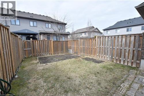 Private backyard with wood fencing, featuring a grass lawn, two raised garden beds, and a brick paver pathway - 52 Meadowridge Street, Kitchener, ON 