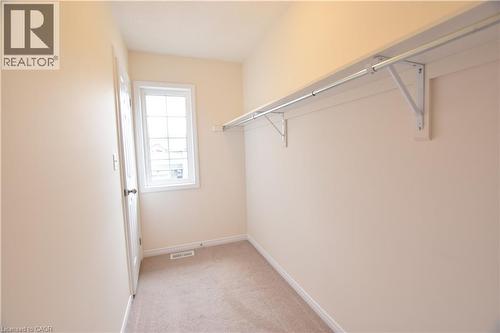 Walk-in closet featuring light beige carpeting, a single window, a baseboard register, a white door, and a built-in rod with shelving - 52 Meadowridge Street, Kitchener, ON 