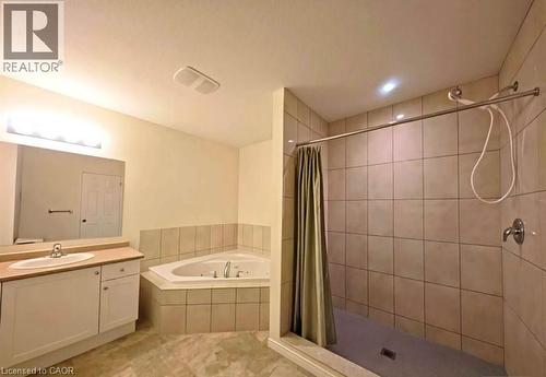Spacious bathroom featuring a corner jetted tub, a separate tiled shower with built-in bench, a single vanity with a large mirror, and tiled flooring - 52 Meadowridge Street, Kitchener, ON 