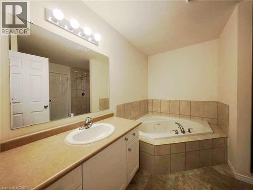 Bathroom featuring a built-in jetted tub with tile surround, a single vanity with an integrated sink, a large wall-mounted mirror, and a chrome light fixture - 52 Meadowridge Street, Kitchener, ON 