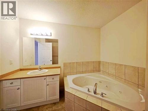Bathroom featuring a corner jetted tub with tiled surround, a light wood-finish vanity with an integrated sink, a large wall-mounted mirror, and overhead strip lighting - 52 Meadowridge Street, Kitchener, ON 