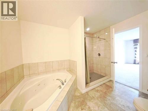 Bathroom featuring a tiled soaking tub with integrated jets, a tiled shower enclosure, and light-toned flooring - 52 Meadowridge Street, Kitchener, ON 
