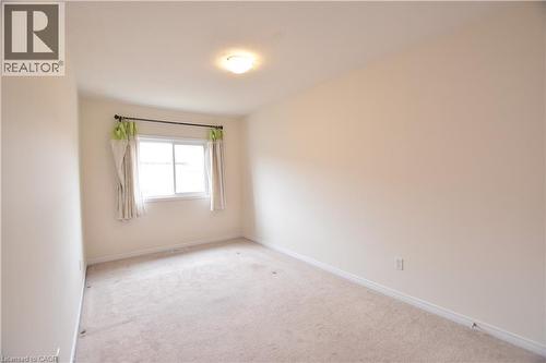 Carpeted room featuring a double-hung window with a dark curtain rod, neutral wall paint, white trim, and an overhead flush-mount light fixture - 52 Meadowridge Street, Kitchener, ON 