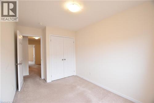 Carpeted room featuring a double-door closet with polished chrome hardware, neutral wall tones, and a ceiling-mounted light fixture - 52 Meadowridge Street, Kitchener, ON 