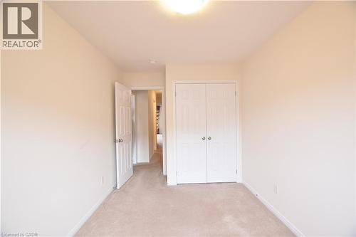 Neutral-toned room featuring carpet flooring, crisp white trim, and a double-door closet with polished hardware - 52 Meadowridge Street, Kitchener, ON 