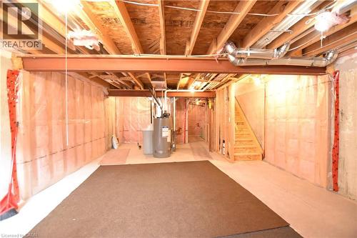 Unfinished lower level featuring an exposed ceiling with wood joists and steel beams, framed wall studs, a water heater, and a wood staircase - 52 Meadowridge Street, Kitchener, ON 