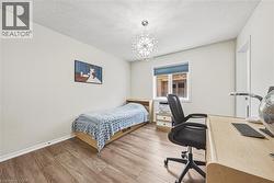 Room featuring wood-finish flooring, a contemporary chandelier, a window with a roller blind, and light-toned walls - 