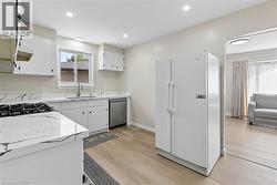 Modern kitchen featuring white cabinetry, stone-finish countertops with dark veining, stainless steel sink with a gooseneck faucet, a built-in gas range, and wood-finish flooring - 