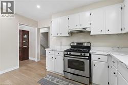 Kitchen featuring white cabinetry with black hardware, stainless steel gas range, coordinating range hood, and white countertops with dark veining - 