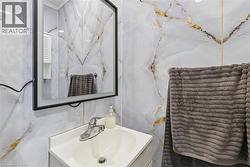Bathroom featuring large-format wall tiles with gold veining, a wall-mounted lighted mirror with a black frame, and a vanity with an integrated sink and chrome faucet - 