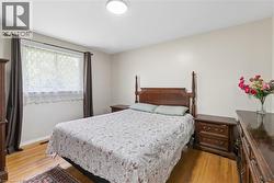 Bedroom featuring wood-finish flooring, a window with curtains, and a ceiling-mounted light fixture - 