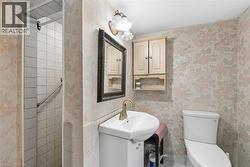 Bathroom featuring a walk-in shower with white tile surround and grab bar, a vanity with an integrated sink and brass-toned faucet, a wall-mounted medicine cabinet, and a toilet - 