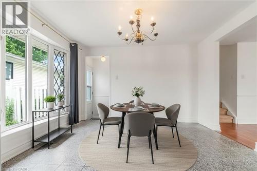 Bright dining area featuring a brass chandelier, large bay window with diamond-patterned panes, white walls, and a combination of stone-look tile flooring and wood-finish flooring - 1259 Ernest Avenue, London, ON - Indoor Photo Showing Dining Room