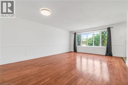 Spacious room featuring wood-finish flooring, white walls with wainscoting, and a large bay window with decorative grilles - 1259 Ernest Avenue, London, ON - Indoor Photo Showing Other Room
