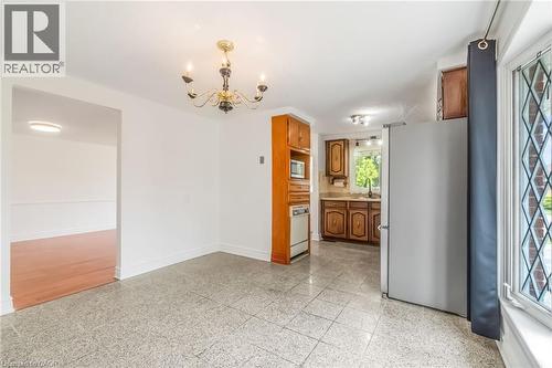 Kitchen and dining area featuring speckled tile flooring, a brass chandelier, wood cabinetry, built-in microwave, and a bay window with decorative grilles - 1259 Ernest Avenue, London, ON - Indoor