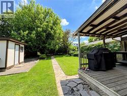 Spacious backyard featuring a covered wood deck, expansive lawn, stone pathway, and a detached storage shed with stucco siding - 