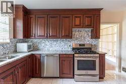 Kitchen featuring rich wood cabinetry, stone countertops, stainless steel appliances, a mosaic tile backsplash, and ceramic tile flooring - 