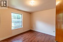 Room featuring wood-finish flooring, a single window with exterior tree-line visibility, and an overhead light fixture - 