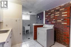 Laundry area featuring a utility sink, a multi-tone brick accent wall, tiled flooring, and a window for natural light - 