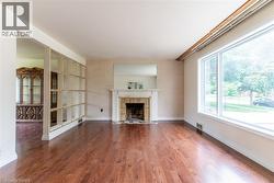 Spacious living area featuring polished wood-finish flooring, a prominent fireplace with a white mantel, and a large picture window - 
