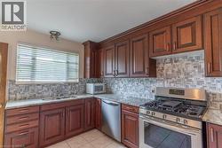 Kitchen featuring cherry wood cabinetry, light-toned granite countertops, a mosaic tile backsplash, stainless steel appliances, and tile flooring - 