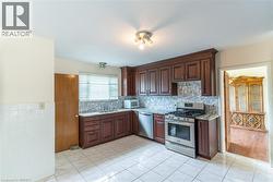 Kitchen featuring dark wood cabinetry, stainless steel appliances, a mosaic tile backsplash, and light-toned tile flooring - 