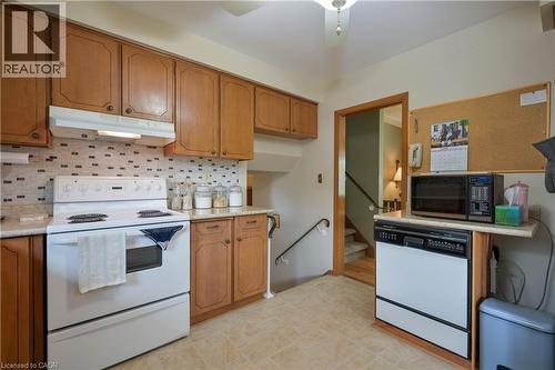 Kitchen featuring wood-finish cabinetry, patterned tile backsplash, and a white electric range - 99 Lorraine Avenue, Kitchener, ON - Indoor Photo Showing Kitchen
