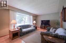 Spacious living area featuring light wood-finish flooring, a large picture window with sheer drapes, and a neutral wall color palette - 