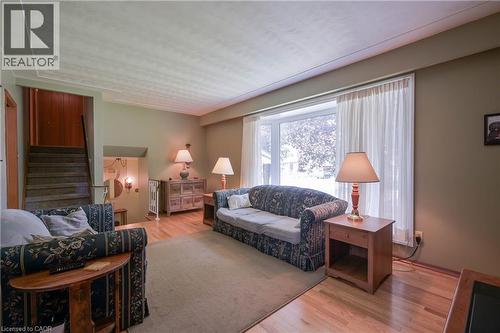 Spacious living area featuring light wood-finish flooring, a large bay window, and a broad staircase with wood paneling - 99 Lorraine Avenue, Kitchener, ON - Indoor