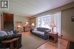 Spacious living area featuring light wood-finish flooring, a large bay window, and a broad staircase with wood paneling - 