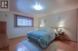 Bedroom featuring warm wood-finish flooring, a large window with vertical blinds, a flush mount ceiling light, and light-toned walls - 