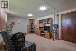 Lower level room featuring a brick corner fireplace with a wood-burning stove, carpet flooring, a drop ceiling, and recessed lighting - 