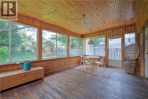 Sunroom featuring extensive natural wood paneling, wood-finish flooring, multiple large windows, and a screened door providing exterior access - 99 Lorraine Avenue, Kitchener, ON - Indoor