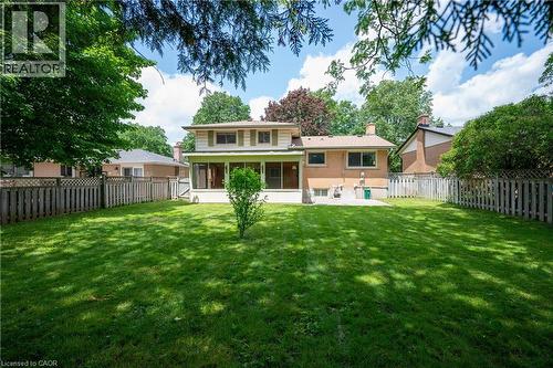 Expansive green lawn with mature perimeter trees, featuring a screened-in porch, a ground-level patio, and wood fencing - 99 Lorraine Avenue, Kitchener, ON - Outdoor