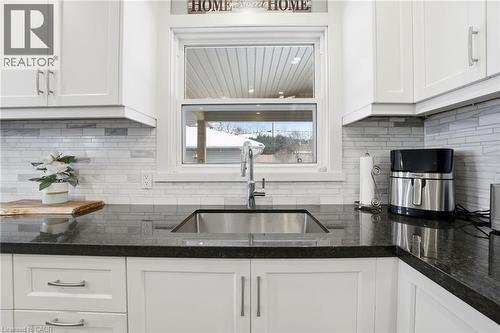 Kitchen with white cabinets, dark stone counters, and backsplash - 473 Mohawk Road W, Hamilton, ON 