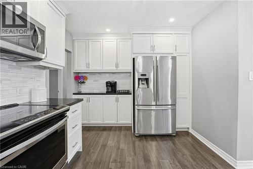 Kitchen featuring stainless steel appliances, white cabinetry, dark wood finished floors, recessed lighting, and backsplash - 473 Mohawk Road W, Hamilton, ON 